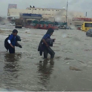 طلاب يعبرون الشارع الغارق بمياه الأمطار