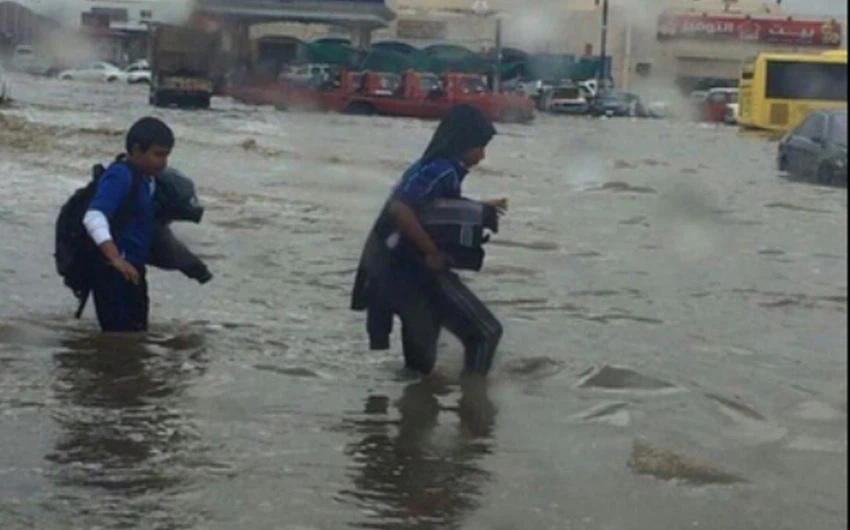 طلاب يعبرون الشارع الغارق بمياه الأمطار